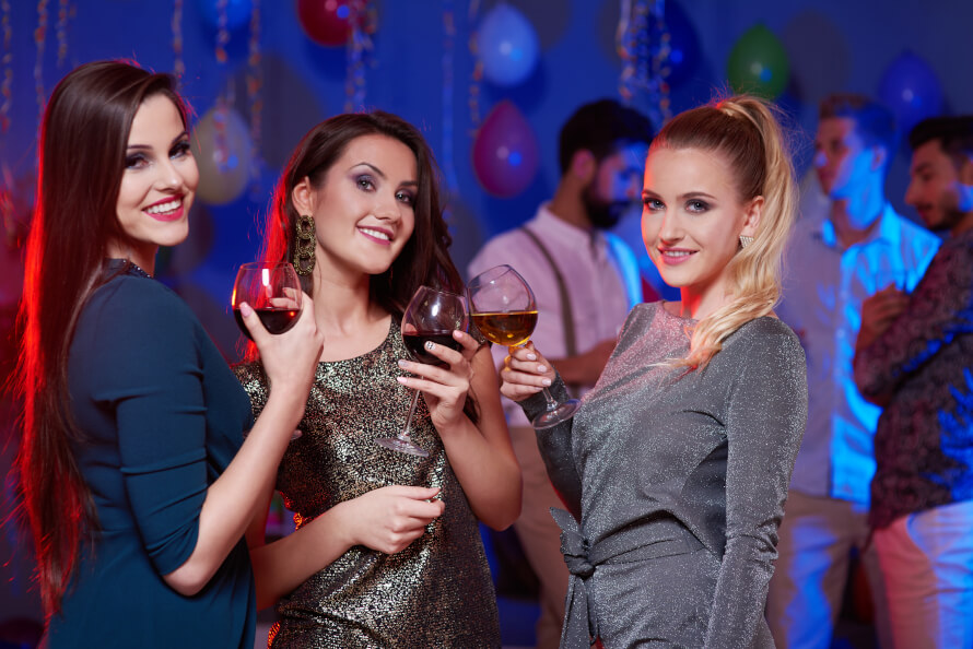 Kobiety w eleganckich sukniach trzymające lampę wina na imprezie firmowej